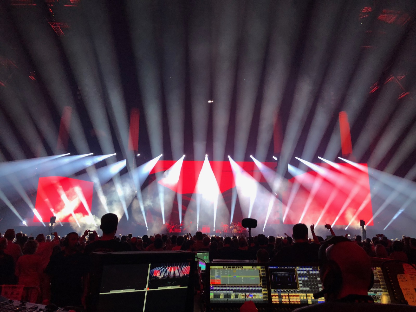 Red-lit stadium show with white beam fans, seen from the front-of-house position