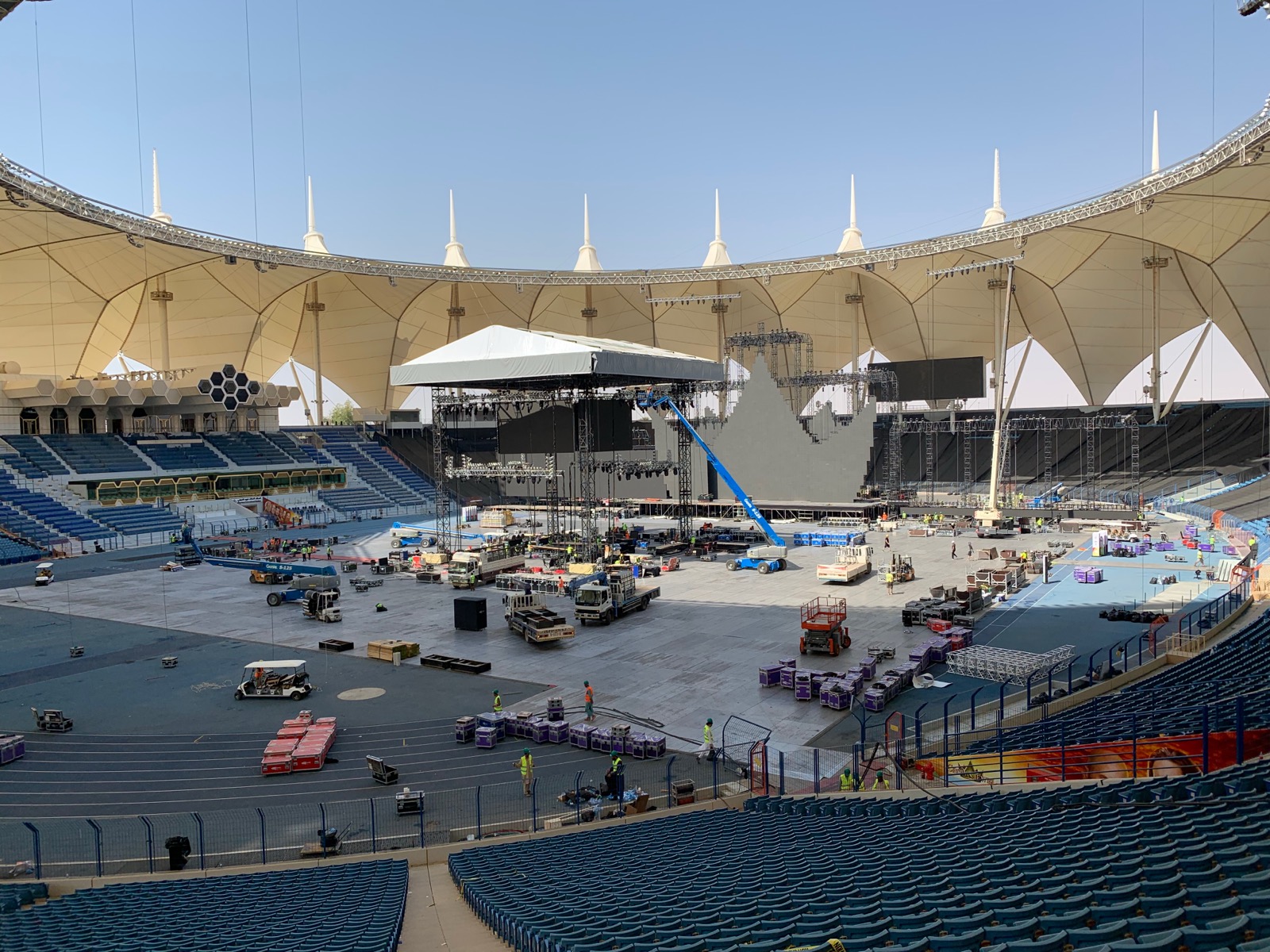Stadium being built for a show, with stage, rigging and access machinery across the arena floor